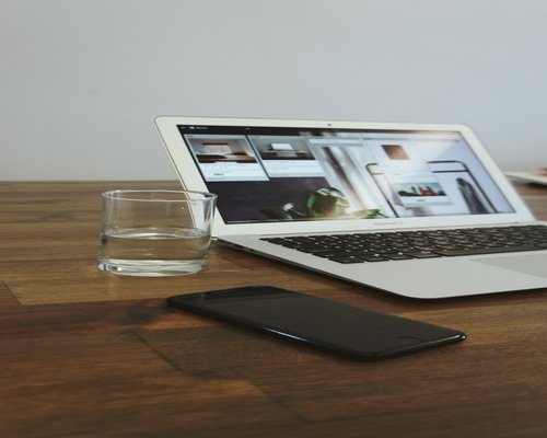 A laptop on a clean wooden table with a glass of pure drinking water nearby